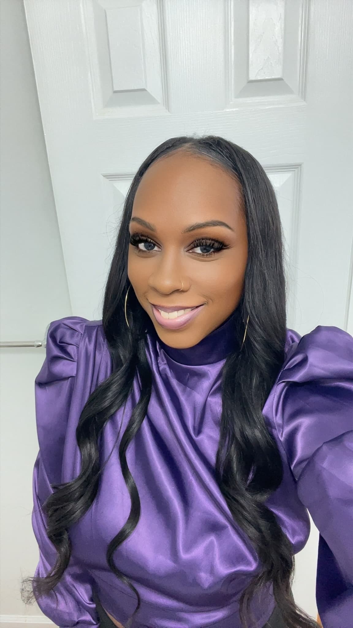 Smiling Black woman with long dark hair wearing a shiny purple satin puff-sleeve blouse.